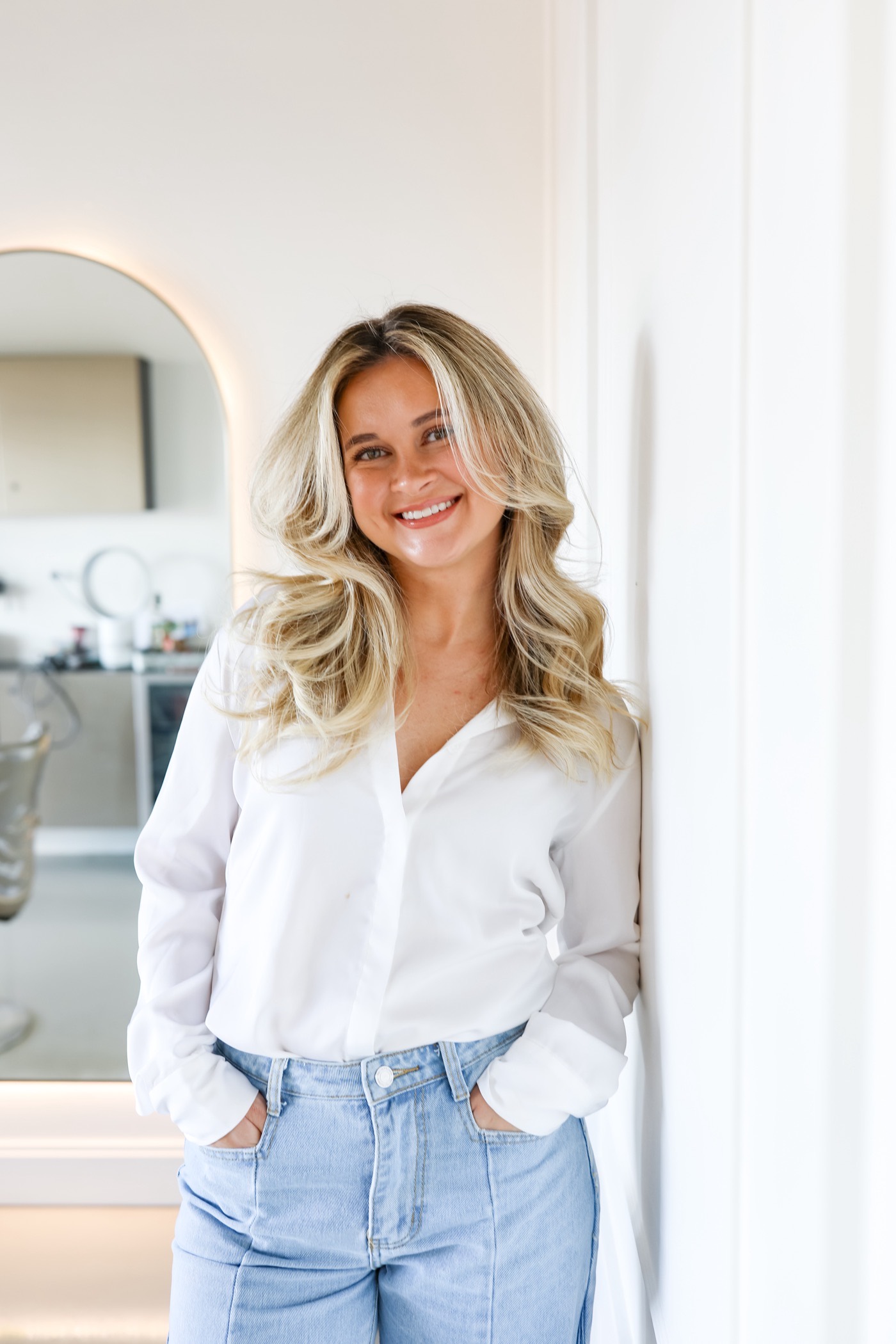 Portrait of a woman in a white shirt leaning against a wall in soft daylight
